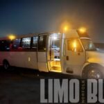 White 30-passenger party bus illuminated at night, showcasing luxury features for events, proms, and group travel in Norfolk.