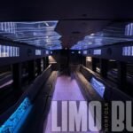 Elegant white-lit ceiling design in a 50-passenger luxury party bus, with black leather wraparound seating and premium entertainment features.